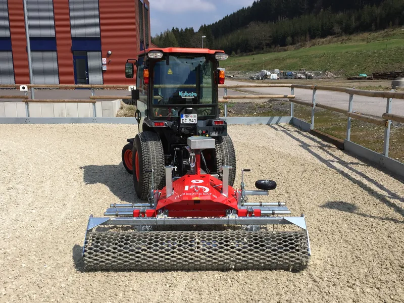 Floor-Care ONE manegevlakker achter een trekker in een buitenbak in daglicht